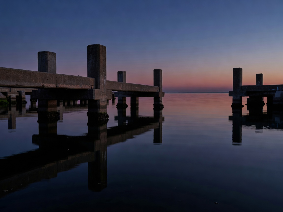 Concrete marine dock structures reflecting in dark water at dusk with glowing beacons